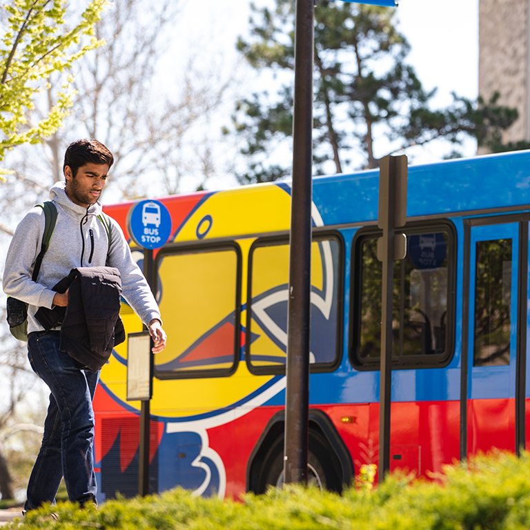 man walking on campus past bus